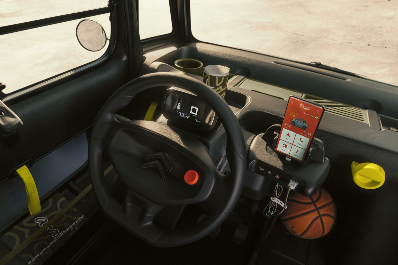The dashboard of a Citroën Ami EV, with a red Flic button integrated on the steering wheel hub and the My Ami Play companion app on the dock.