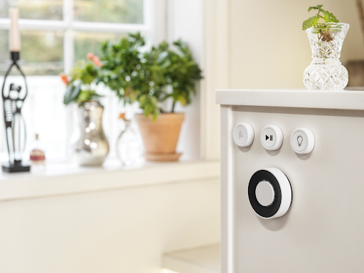 A Flic Smart Button beside a Flic Twist remote on a wooden cabinet.