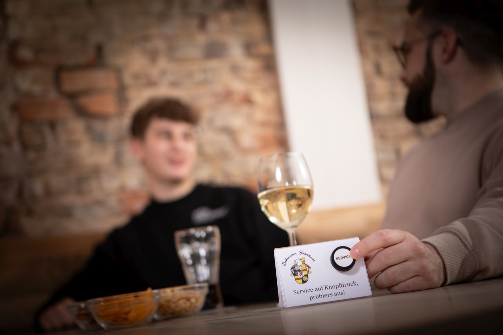 Two patrons at a brick-walled restaurant with a Flic service button on the table.