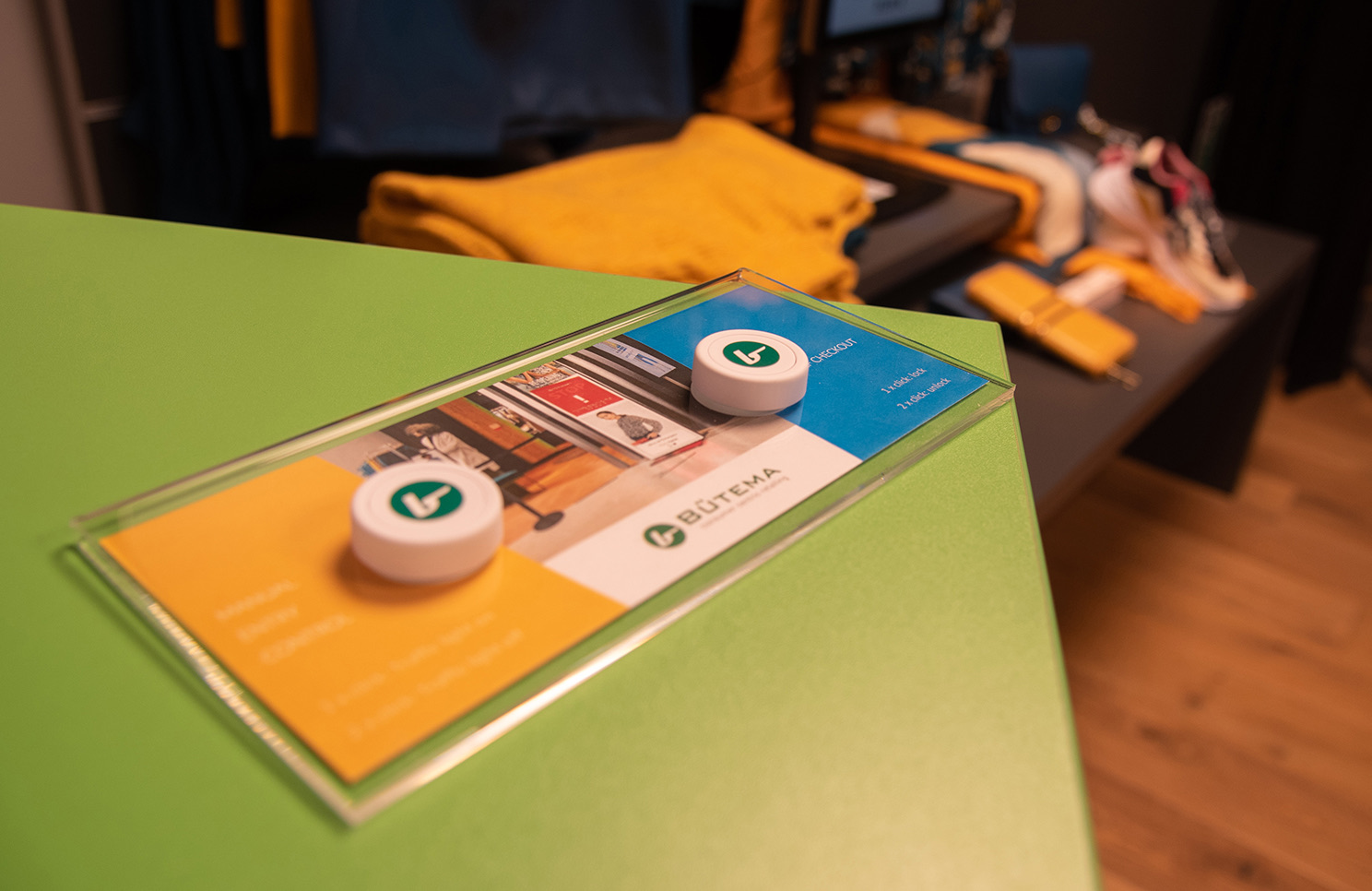 Two Flic Smart Buttons on a green retail counter at a Bütema fitting-room demo, with the Bütema branded card describing checkout and assistance triggers.