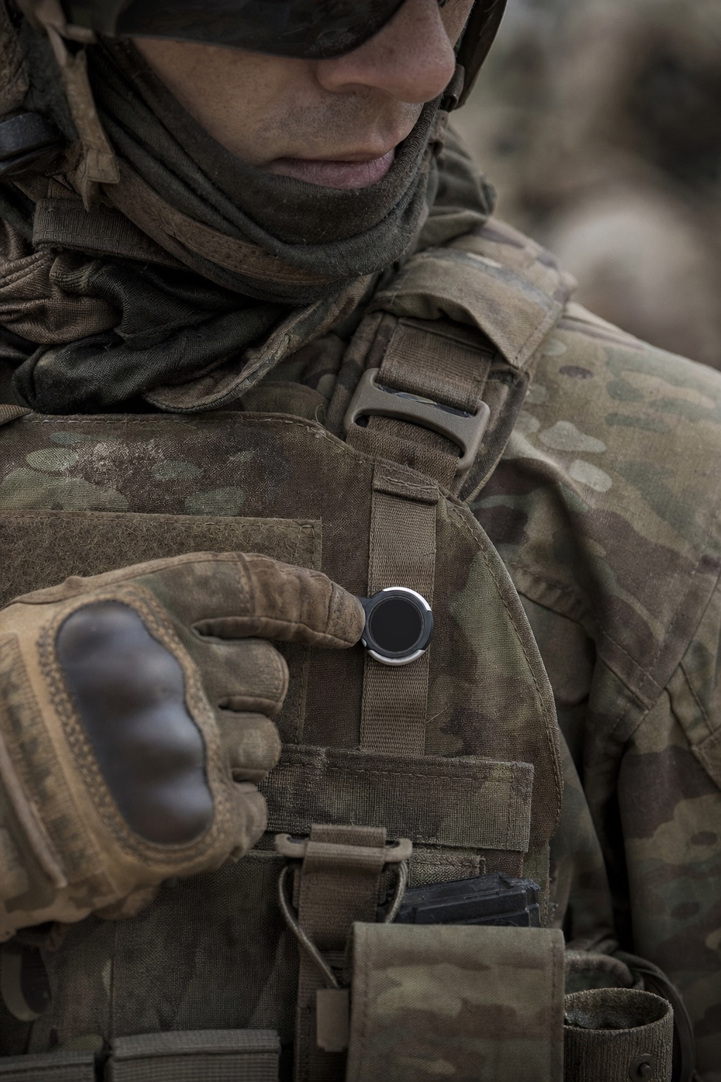 A gloved hand reaching for a Flic Smart Button mounted on the front MOLLE webbing of a multicam plate carrier.