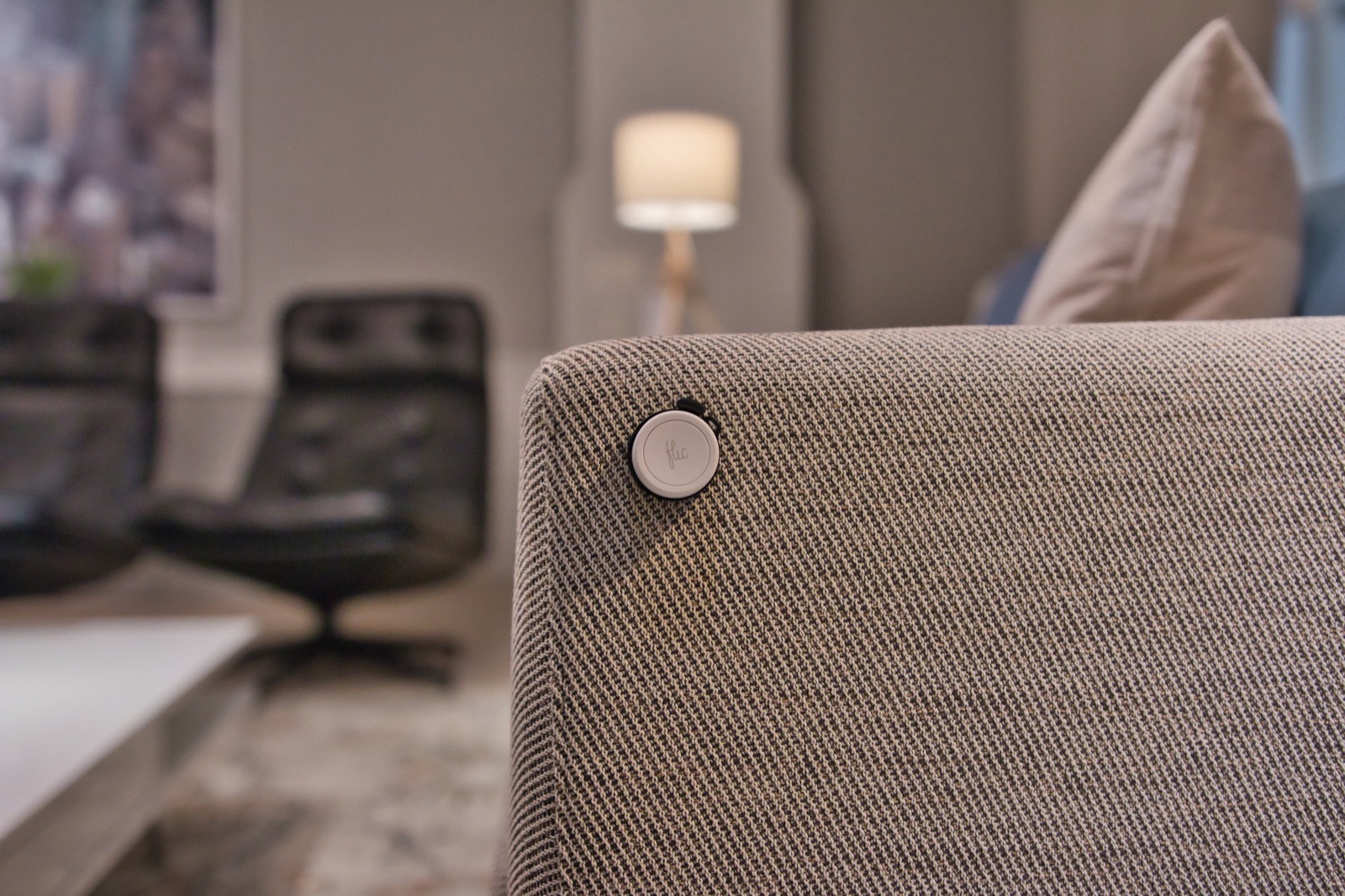 A Flic button mounted to the textured fabric of a sofa in a refined living room.