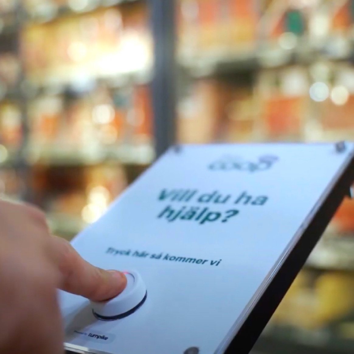 A customer pressing a Coop service-call button labelled "Vill du ha hjälp?" in Swedish — a Turnpike-powered Flic deployment in a grocery aisle.
