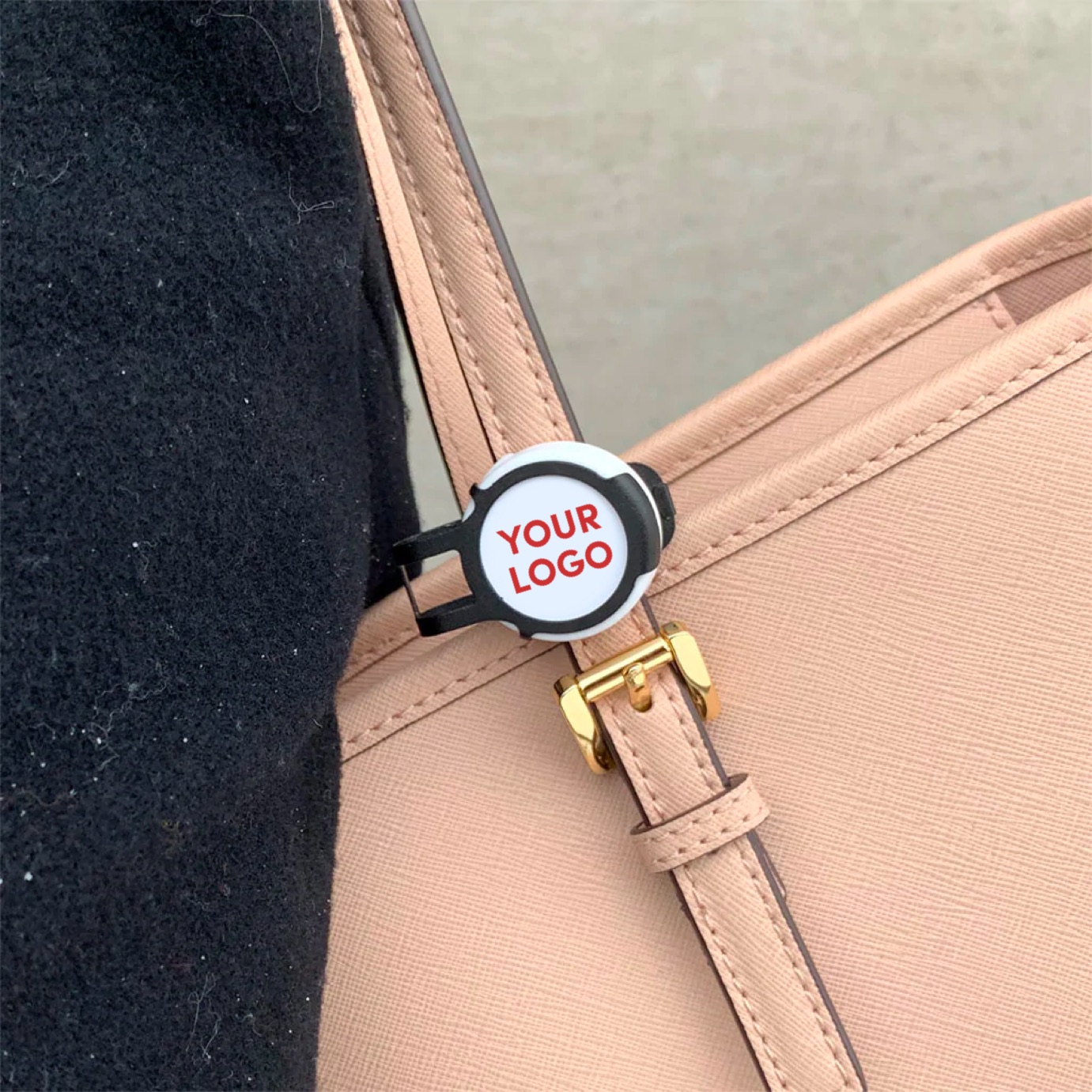 A custom-branded white-label Flic safety button with "Your Logo" face, clipped discreetly to the strap of a leather handbag.