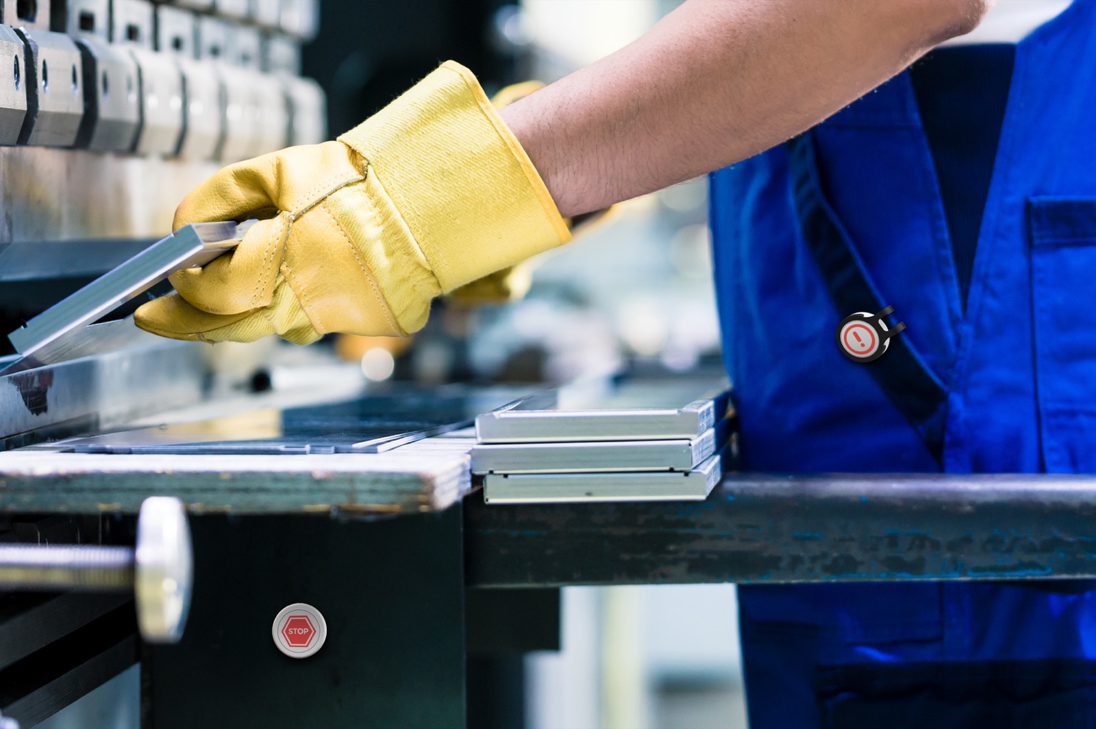 An industrial worker in blue overalls and yellow safety gloves on a press, with a Flic safety button clipped to the chest strap.